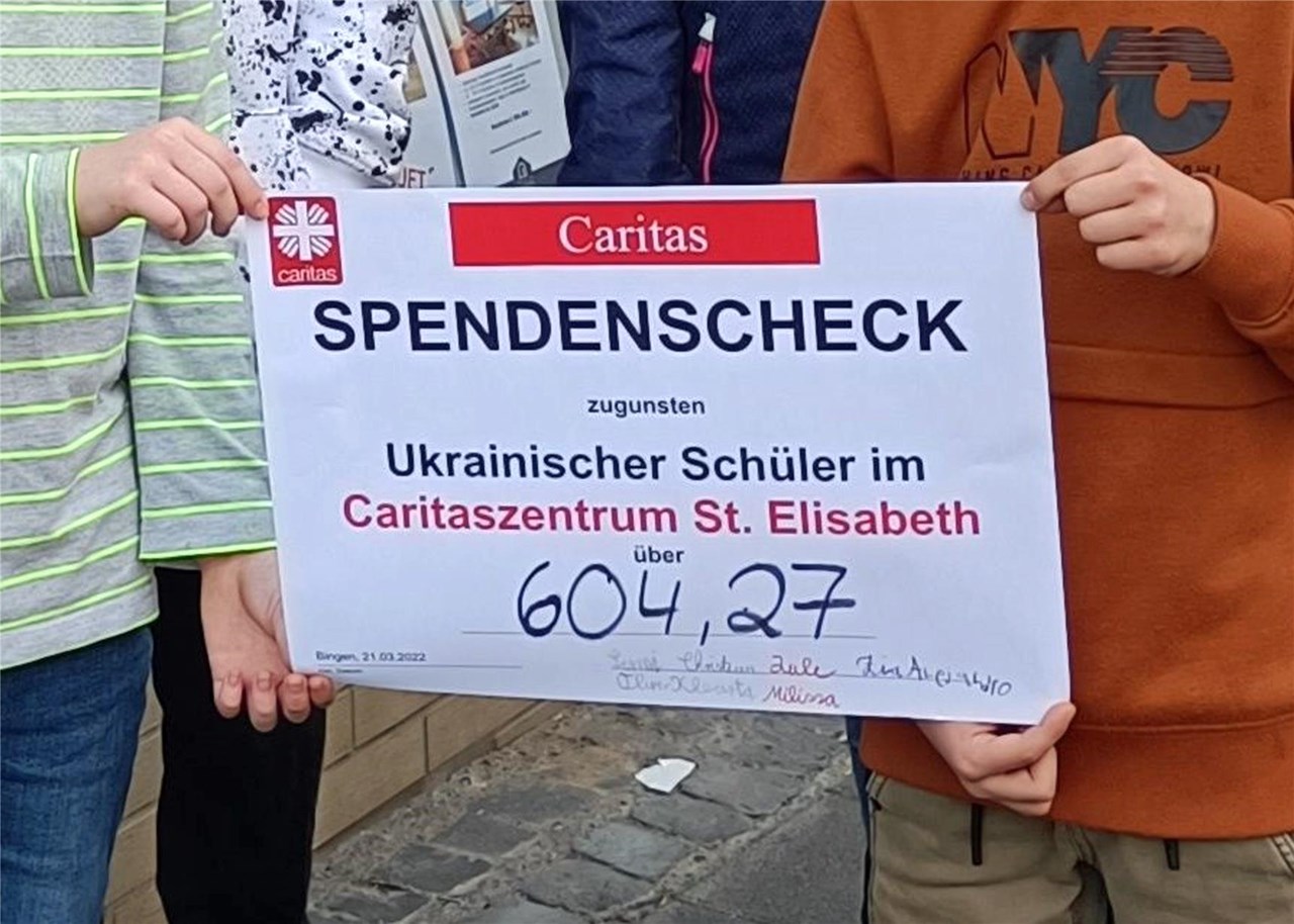 Vier Hände halten einen Spendenscheck über die Summe von 604,27 Euro